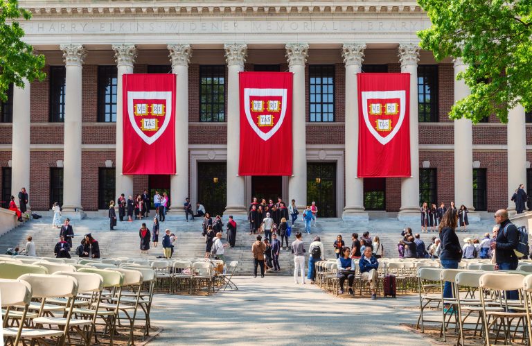 Cambridge, Massachusetts — May 22, 2023: Students in graduation gowns and families in front of the Harry Elkins Widener Memorial Library. Harvard VERITAS banners hang in front of building. The library houses some 3.5 million books in its stacks and is the center­piece of the Harvard College Libraries. It honors 1907 Harvard College graduate and book collector Harry Elkins Widener.