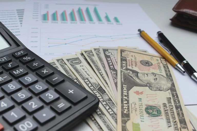 Close-up of American dollars with calculator and pens over documents on table.