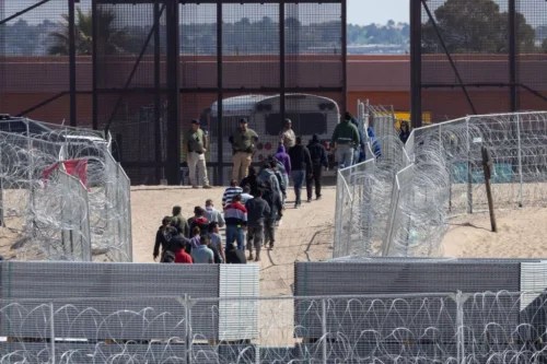 A group of migrants walk through the road as a border police stand guard following hundreds of migrants' descent from the train toward the Mexico-U.S. border in Ciudad Juarez, Mexico, April 22, 2024. (David Peinado / Anadolu via Getty Images)