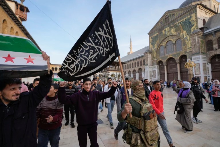 A masked opposition fighter carries a flag of Hayat Tahrir al Sham in the courtyard of the Umayyad Mosque in the old walled city of Damascus, Syria, Tuesday, Dec. 10, 2024.