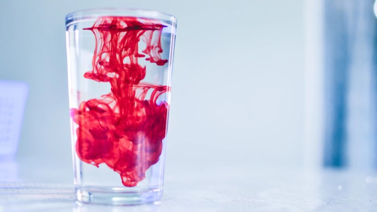 Dispersing red dye in a glass of water with space for text.