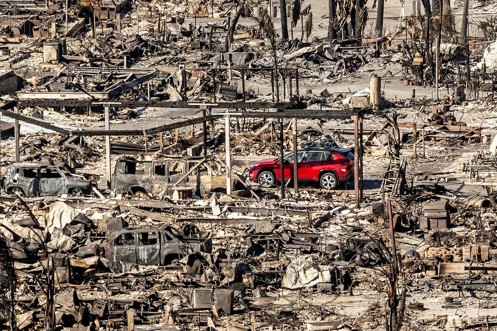 A car drives past homes and vehicles destroyed by the Palisades fire at the Pacific Palisades Bowl Mobile Estates, Sunday, Jan. 12, 2025, in Los Angeles.
