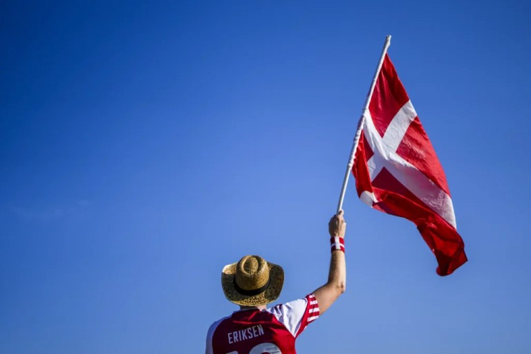 A Denmark's soccer team supporter waves the national flag as he waits for friends outside the stadium ahead of the Group C match between the Denmark and Serbia at the Euro 2024 soccer tournament in Munich, Germany, Tuesday, June 25, 2024.