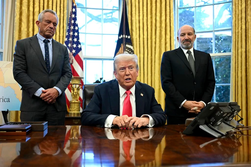 President Donald Trump speaks to reporters before signing an executive order as Health and Human Services Secretary Robert F. Kennedy Jr., left, and Commerce Secretary Howard Lutnick listen in the Oval Office at the White House in Washington, Tuesday, Feb. 25, 2025. (Pool via AP)