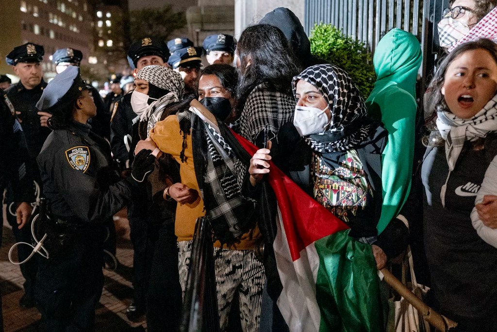 People hold their ground near a main gate at Columbia University in New York, Tuesday, April 30, 2024, as New York City police officers move to clear the area after a building was taken over by protesters earlier today. Colleges and universities have long been protected places for free expression without pressure or punishment. But protests over Israel's conduct of the war in Gaza in its hunt for Hamas after the Oct. 7 massacre has tested that ideal around the world.