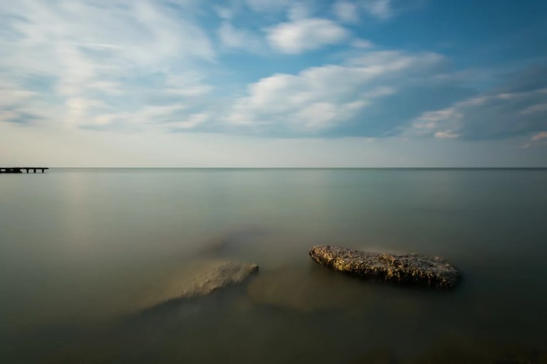Calm freshwater of the lake Eerie in the morning. blue sky with white clouds photographed at slow shutter. rocks peaking from below the surface of the lake.