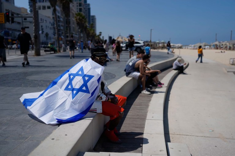 Draped in an Israeli flag, a man sits on the edge of a beach during Israel's Independence Day celebrations in Tel Aviv, Tuesday, May 14, 2024. Israelis are marking 76 years since Israel's creation.
