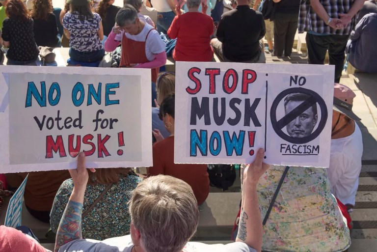 People hold up sign as they attend a town hall by U.S. Rep. Ro Khanna (D-CA) for the residents of the CA-41st district at Norco College Amphitheater in Norco, Calif., one of a series of town halls across three California Congressional districts held by Republicans, on Sunday, March 23, 2025. (AP Photo/Damian Dovarganes)
