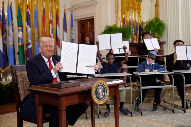 President Donald Trump, left, holds up a signed executive order as young people hold up copies of the executive order they signed at an education event in the East Room of the White House in Washington, Thursday, March 20, 2025.