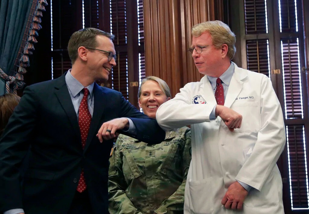 Texas Education Agency commissioner Mike Morath, left, and Dr. David Flegger, right, bump elbows rather that shake hands before a coronavirus update from Texas Gov.Greg Abbott, Friday, March 13, 2020, in Austin, Texas.  Abbott declared a state of disaster Friday as the coronavirus pandemic spread to all of the state's biggest cities.