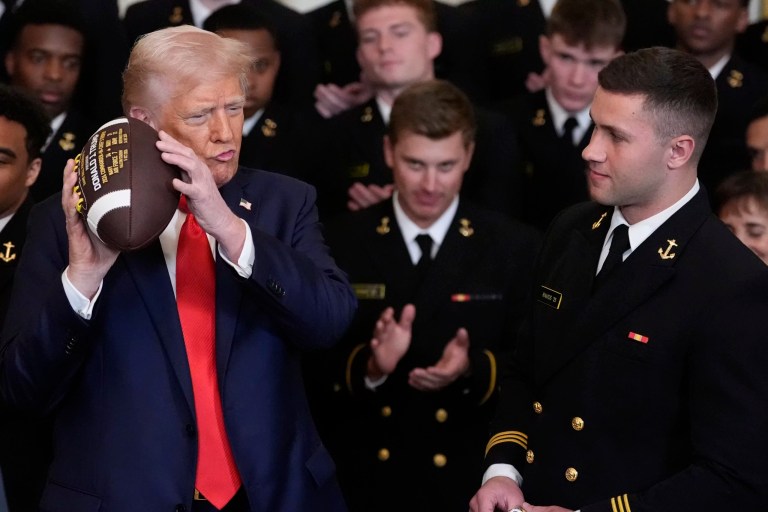 President Donald Trump holds a football as Colin Ramos watches during the Commander innChief trophy presentation to the Navy Midshipman football team in the East Room of the White House, Tuesday, April 15, 2025, in Washington.