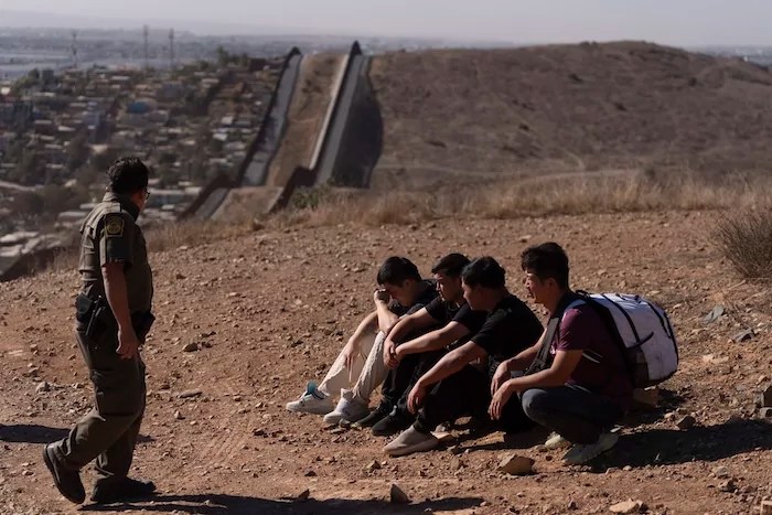 A Border Patrol agent walks past four men being detained after crossing the border through a gap in the walls separating Mexico and the United States, Jan. 23, 2025, in San Diego.