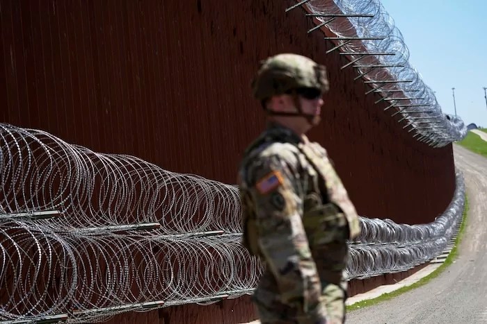 A member of the military looks on in front of newly-installed concertina wire lining one of two border walls separating Mexico from the United States during a news conference on joint operations involving the military and the Border Patrol Friday, March 21, 2025, in San Diego. (AP Photo/Gregory Bull)