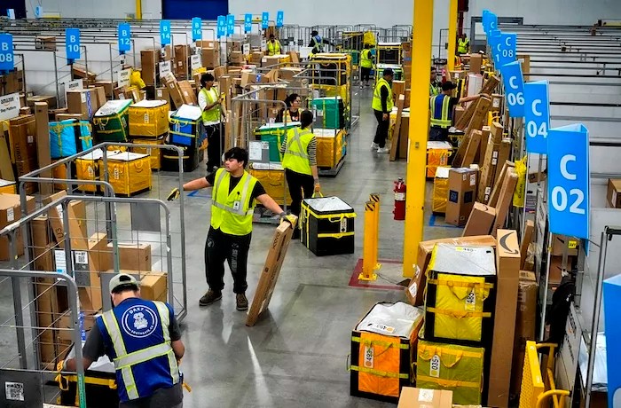 FILE - Amazon employees load packages on carts before being put on to trucks for distribution for Amazon's annual Prime Day event at an Amazon's DAX7 delivery station on Tuesday, July 16, 2024, in South Gate, Calif.