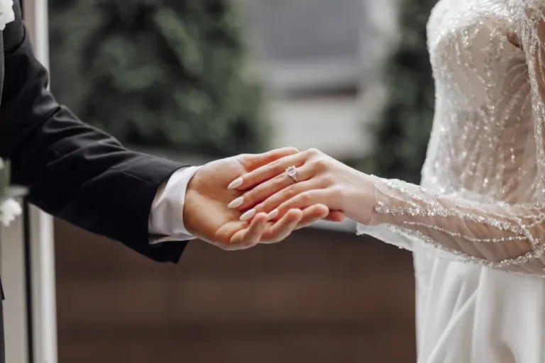 A man gently holds a bride's hand with a gold wedding ring.