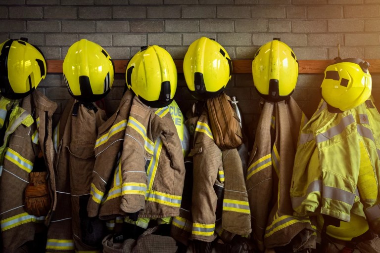 Firefighting gear including helmets, gloves, protection jacket and trousers among other clothing and equipment in fire station.