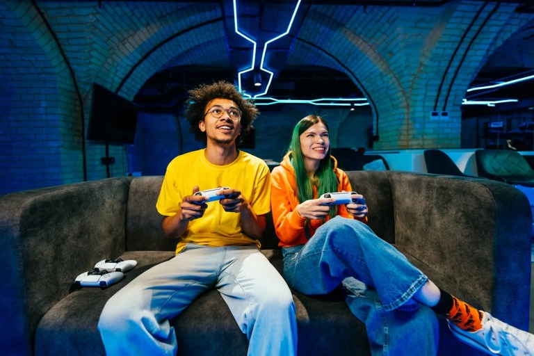 Multiethnic group of young friends playing videogames at home sitting on the sofa - Videogamers having fun playing e-sports at computer videogame console