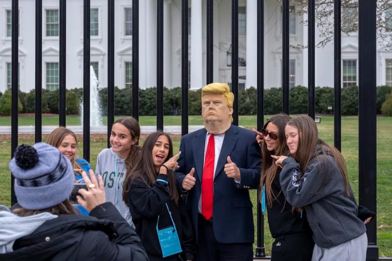 A group of young visitors pose for a photo with another visitor to the city wearing a mask of President Donald Trump in front of the White House in Washington, Thursday, March 13, 2025.