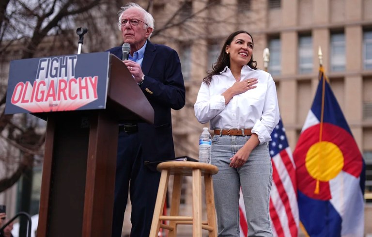 Sen. Bernie Sanders, I-Vt., left, speaks as Rep. Alexandria Ocasio-Cortez, D-N.Y., responds to calls of support during a stop of their 