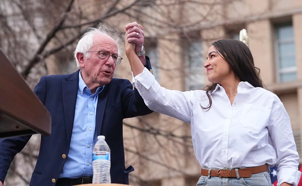 Sen. Bernie Sanders, I-Vt., left, greets Rep. Alexandria Ocasio-Cortez, D-N.Y., as they speak during a stop of their "Fighting Oligarchy" tour that filled Civic Center Park, Friday, March 21, 2025, in Denver.