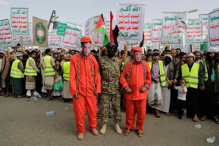 Houthi supporters perform an officer stands between two individuals wearing red prison uniforms and face masks depicting Israeli Prime Minister Benjamin Netanyahu, left, and U.S. President Donald Trump, during a weekly anti-U.S. and anti-Israel rally in Sanaa, Yemen, Friday, May 9, 2025.