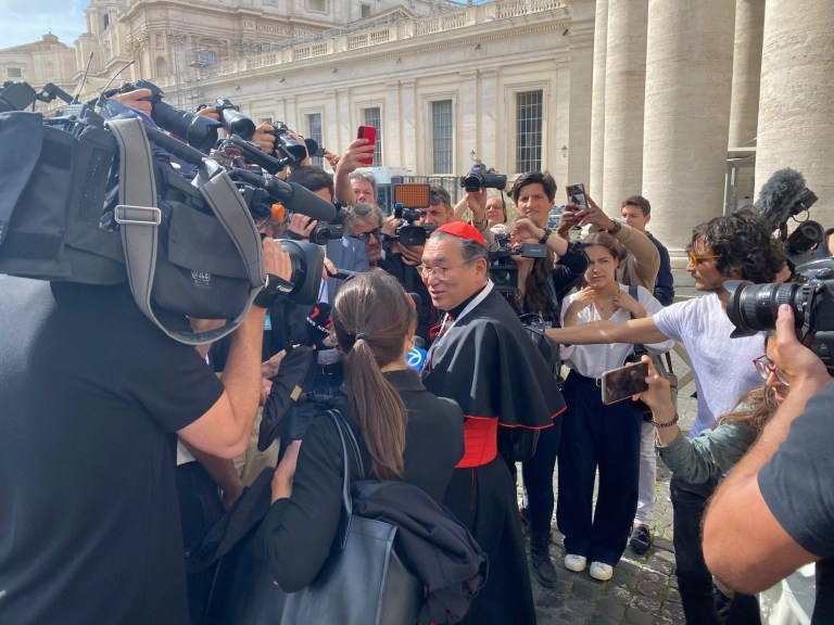 Cardinal Isao Kikuchi of the Archdiocese of Tokyo is surrounded by journalists as he walks toward the Vatican down Via Paolo VI just outside the city-state's limits. He gave curt, muted answers as he attempted to push his way through the crowd politely.