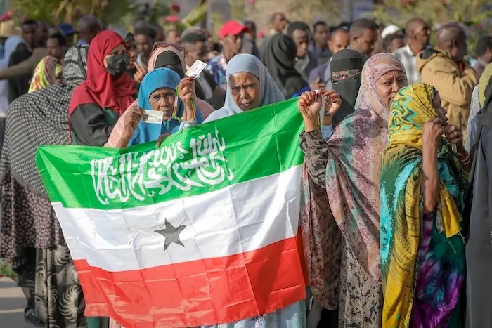 A woman displays the Somaliland flag as people queue to cast their votes during the 2024 Somaliland presidential election at a polling station in Hargeisa, Somaliland, Wednesday, Nov. 13, 2024.