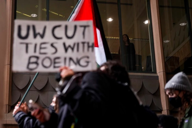 People watch from a nearby building as a protester walks by with a sign calling for the school to cut ties with Boeing during a student-led pro-Palestinian protest at the University of Washington campus Wednesday, Feb. 5, 2025, in Seattle.