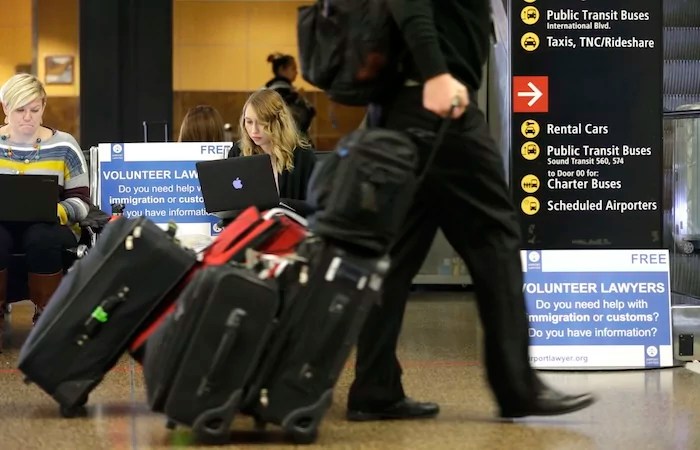 Asti Gallina, center, a volunteer law student from the University of Washington, works at a station near where passengers arrive on international flights at Seattle-Tacoma International Airport Tuesday, Feb. 28, 2017, in Seattle. Gallina was volunteering with the group Airport Lawyer, which also offers a secure website and mobile phone app that alerts volunteer lawyers to ensure travelers make it through customs without trouble. Airport officials and civil rights lawyers around the country are getting ready for President Donald Trump's new travel ban, which is expected to be released as soon as Wednesday. (AP Photo/Ted S. Warren)