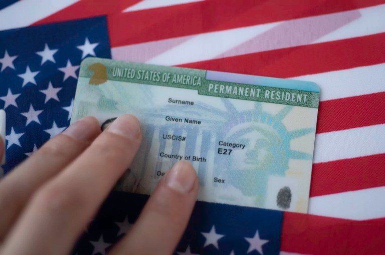Permanent Resident Green Card of United states of America on flag of U.S. Above close up view.