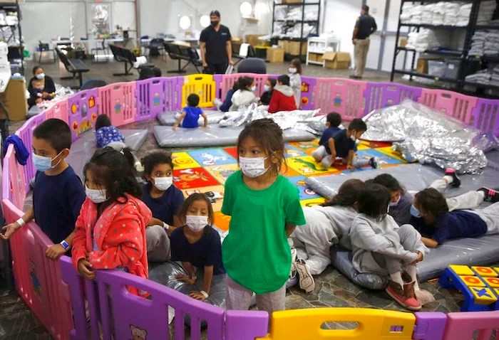 FILE - In this March 30, 2021, file photo, young unaccompanied migrants, from ages 3 to 9, watch television inside a playpen at the U.S. Customs and Border Protection facility, the main detention center for unaccompanied children in the Rio Grande Valley, in Donna, Texas. Migrant families will be held at hotels in the Phoenix area in response to a growing number of people crossing the U.S.-Mexico border, authorities said Friday, April 9, 2021 another step in the Biden administration's rush to set up temporary space for them (AP Photo/Dario Lopez-Mills, Pool, File)
