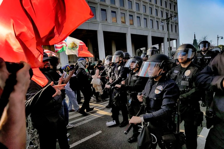 Los Angeles police in riot gear form a skirmish line and push back protesters down a street away from a federal building in downtown Los Angeles
