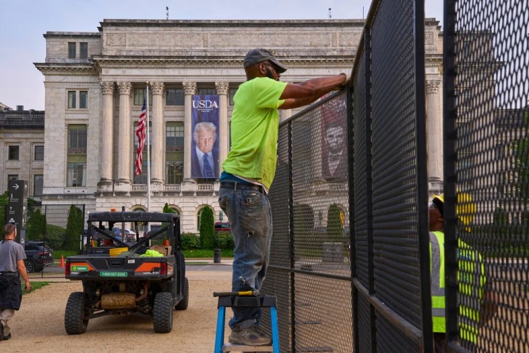 Workers install security fencing on the National Mall, Tuesday, June 10, 2025, outside the USDA Whitten Building where a large photograph of President Donald Trump is draped, in Washington.