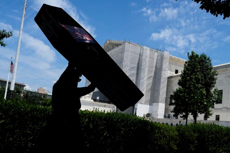 A demonstrator carries a cardboard casket past the Supreme Court in protest of President Donald Trump's tax breaks and spending cuts package, Monday, June 30, 2025, in Washington.