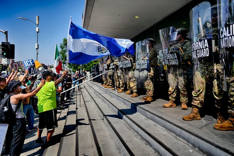 A protester waves a National Flag of El Salvador in front of a line of California National Guard in front of Federal Building on Monday, June 9, 2025, in downtown Los Angeles.