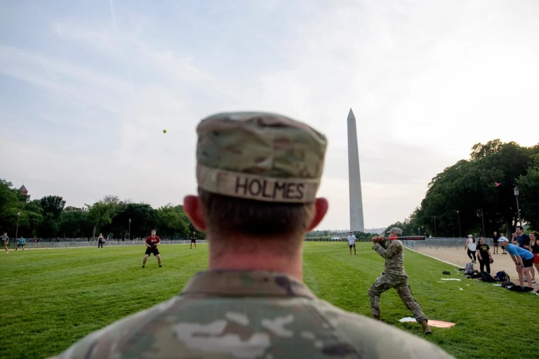 Seen through security fencing, Army Spc. Steven Holmes, left, watches Army Sgt. Chase Beasley, right, take a swing as they sit-in on a game of softball with congressional staffers on the National Mall, during preparations for an upcoming military parade commemorating the Army's 250th anniversary and coinciding with President Donald Trump's 79th birthday, Thursday, June 12, 2025, in Washington.