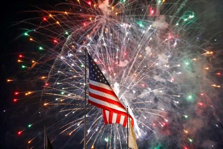 Fireworks explode behind a United States flag during a Fourth of July celebration at State Fair Meadowlands, Saturday, July 4, 2015, in East Rutherford, N.J. (AP Photo/Julio Cortez)