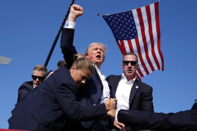 President Donald Trump is surrounded by Secret Service agents after an assassination attempt at a campaign rally.