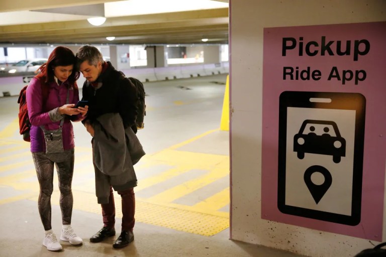 Ann Iturra, left, and Jeremy Reineck huddle over a cell phone as they tried to navigate their rideshare at the Uber & Lyft pickup at Logan Airport after arriving in Boston from Florida on Dec. 23, 2019. The travelers were surprised at how far they had to walk to get to the rideshare location inside Central Parking. The controversial new Logan drop-off rules, the first of their kind in the nation, were approved in April and went fully into effect about two weeks ago - just in time for the holiday travel season. The sequence of frustration, confusion, and acceptance seems to be a common reception for the policy, which consolidated pickups and drop-offs in the airports central garage. (Photo by Jessica Rinaldi/The Boston Globe via Getty Images)