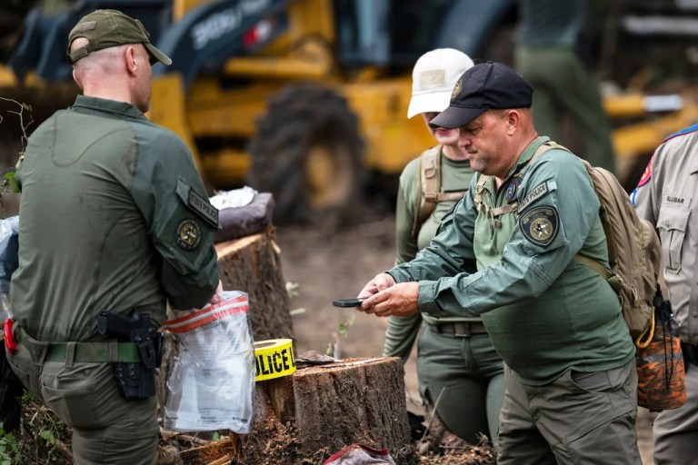 Texas Department of Public Safety Troopers photograph legal documents believed to belong to a body found during search and rescue efforts near the Guadalupe River after a flash flood swept through the area, Monday, July 7, 2025, in Ingram, Texas. (AP Photo/Eli Hartman)