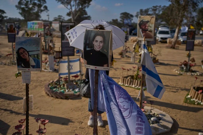 A woman walks with an umbrella reading 'End the war immediately,' during a protest demanding immediate release of hostages held by Hamas in the Gaza Strip, at the site of the Oct. 7, 2023, Hamas attack on the Nova music festival near Kibbutz Re'im in southern Israel, Wednesday, July 2, 2025.