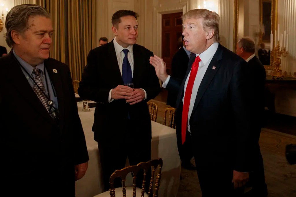 President Donald Trump talks with Tesla and SpaceX CEO Elon Musk, center, and White House chief strategist Steve Bannon during a meeting with business leaders in the State Dining Room of the White House in Washington, Friday, Feb. 3, 2017.