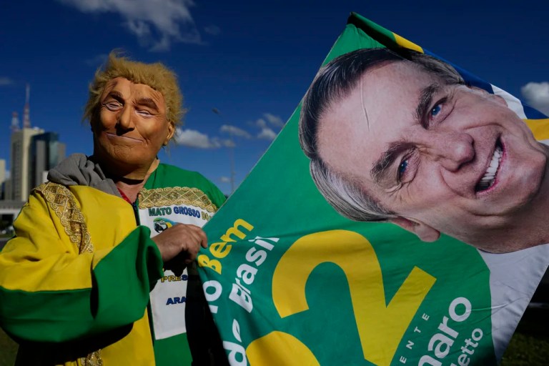 A demonstrator wearing a mask depicting U.S. President Donald Trump holds a flag with the image of former President Jair Bolsonaro, during a rally in support of a proposed bill to grant amnesty to those arrested for storming government buildings in an alleged coup attempt in 2023, in Brasilia, Brazil, Wednesday, May 7, 2025.