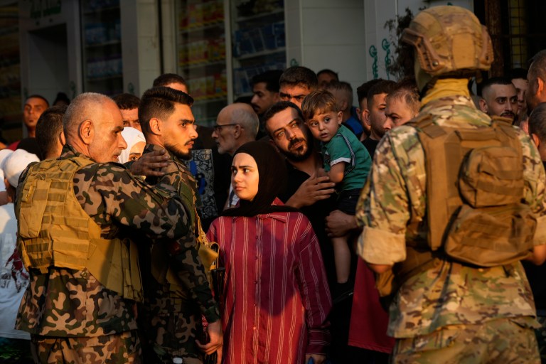 Palestinian gunmen from the National Security Forces, left, and Palestinian citizens, center, look at a Lebanese soldier, right, who blocks the entrance of Burj al Barajneh Palestinian refugee camp, where Palestinian factions handed over weapons to the Lebanese army, in Beirut, Thursday, Aug. 21, 2025.