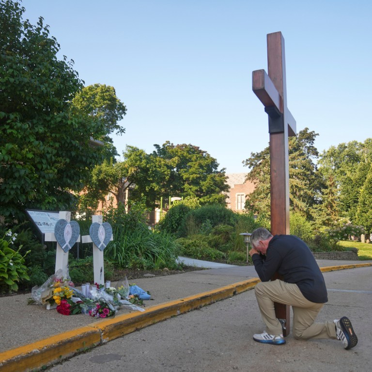 Dan Beazley kneels with a giant cross in front of a memorial at Annunciation Catholic Church after Wednesday's school shooting, Thursday, Aug. 28, 2025, in Minneapolis.