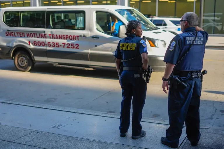 Washington Metropolitan Police officers watch as a shuttle parks outside of Martin Luther King library to make pickups for any individuals that want to be taken to a shelter for the homeless, Thursday, Wednesday, Aug. 13, 2025 in downtown Washington. (AP Photo/Pablo Martinez Monsivais)