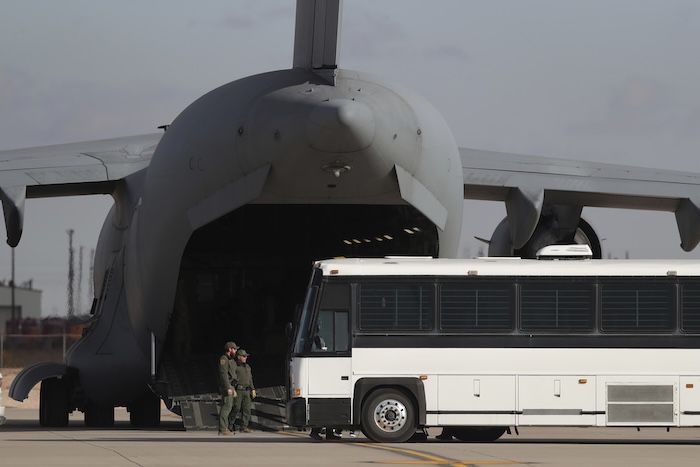 A military aircraft waits for migrants to board from a bus.
