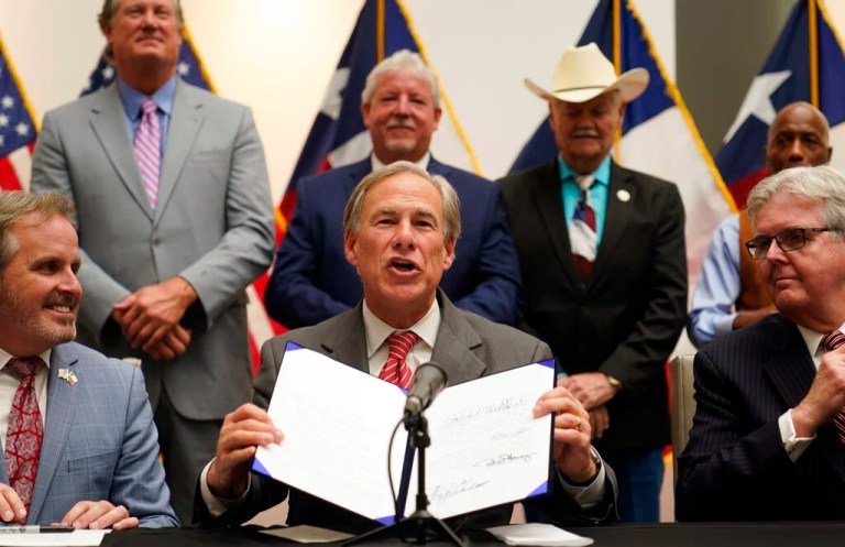 Texas Gov. Greg Abbott (R) shows off his signature after signing Senate Bill 1, also known as the election integrity bill, into law with State Sen. Bryan Hughes (R), front center left, and Lt. Gov. Dan Patrick, front right looking on with others in Tyler, Texas, Tuesday, Sept. 7, 2021.