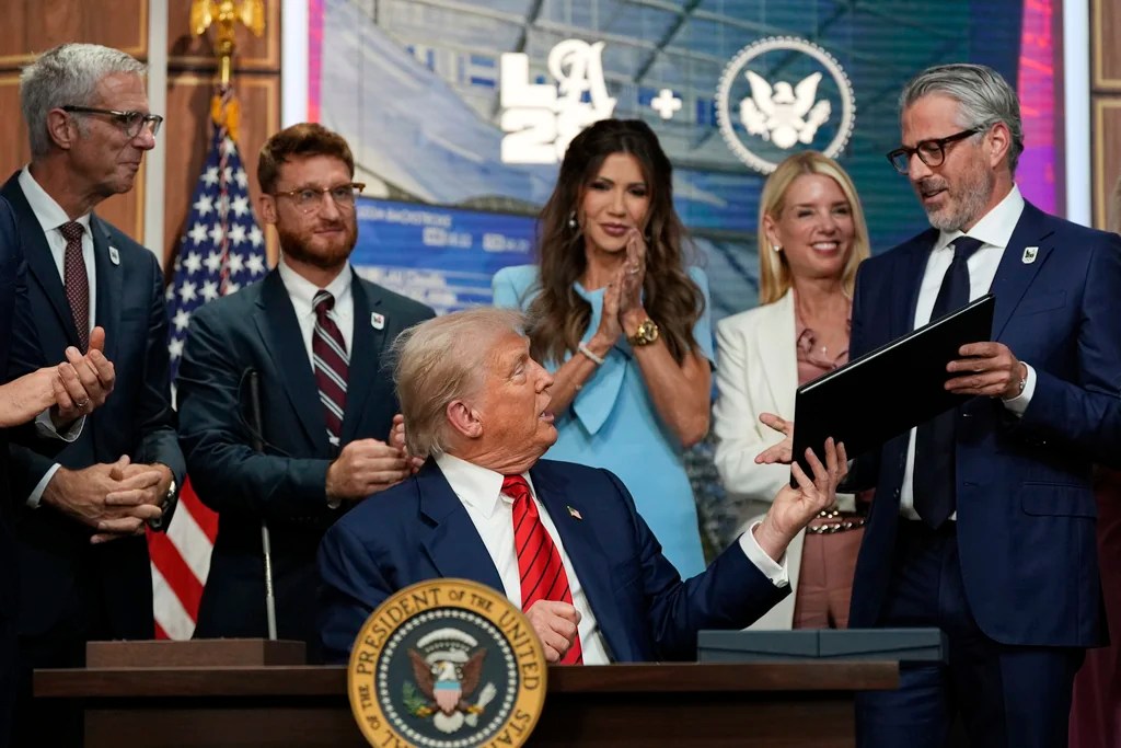 President Donald Trump hands a signed executive order about the 2028 Los Angeles Olympic Games, to Casey Wasserman, chairman of LA28, in the South Court Auditorium of the Eisenhower Executive Office Building on the White House campus, Tuesday, Aug. 5, 2025, in Washington. 