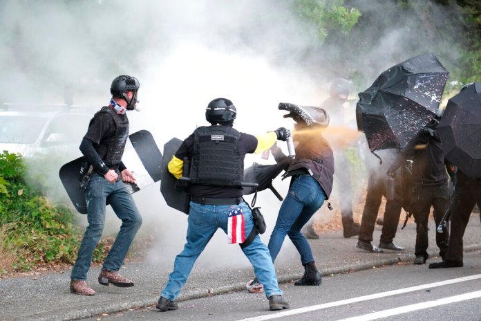 FILE - In this Sunday, Aug. 22, 2021, file photo, members of the far-right group Proud Boys and anti-fascist protesters spray bear mace at each other during clashes between the politically opposed groups in Portland, Oregon. 